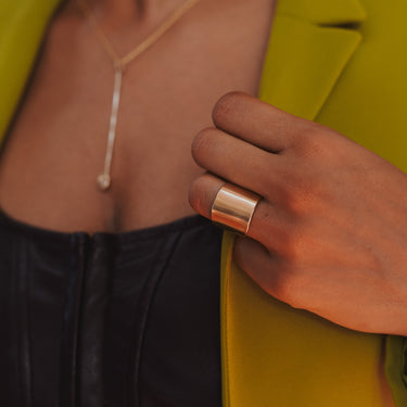 Model hand holds lapel of a yellow green suit jacket and wears a solid saddle ring on their ring finger