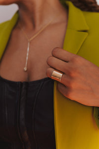 Model hand holds lapel of a yellow green suit jacket and wears a solid saddle ring on their ring finger